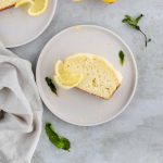 slice of lemon loaf on a white plate and garnished with a fresh slice of lemon and mint.