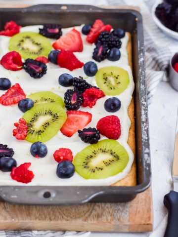 baked fruit pizza topped with frosting and fruit.