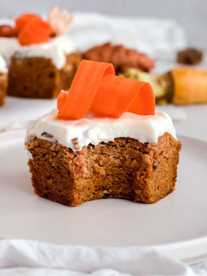 carrot cake bar topped with cream cheese icing and shredded carrots with a bite taken out of it.