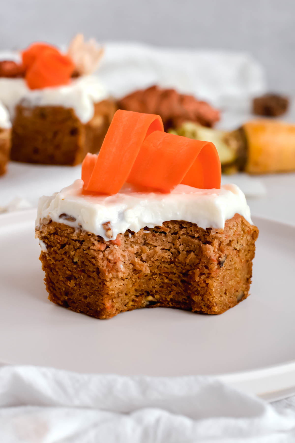 carrot cake bar topped with cream cheese icing and shredded carrots with a bite taken out of it.
