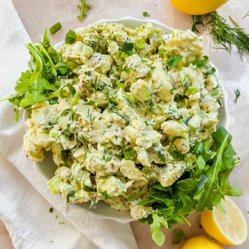 creamy healthy lemon dill potato salad mixed together over arugula in white bowl.