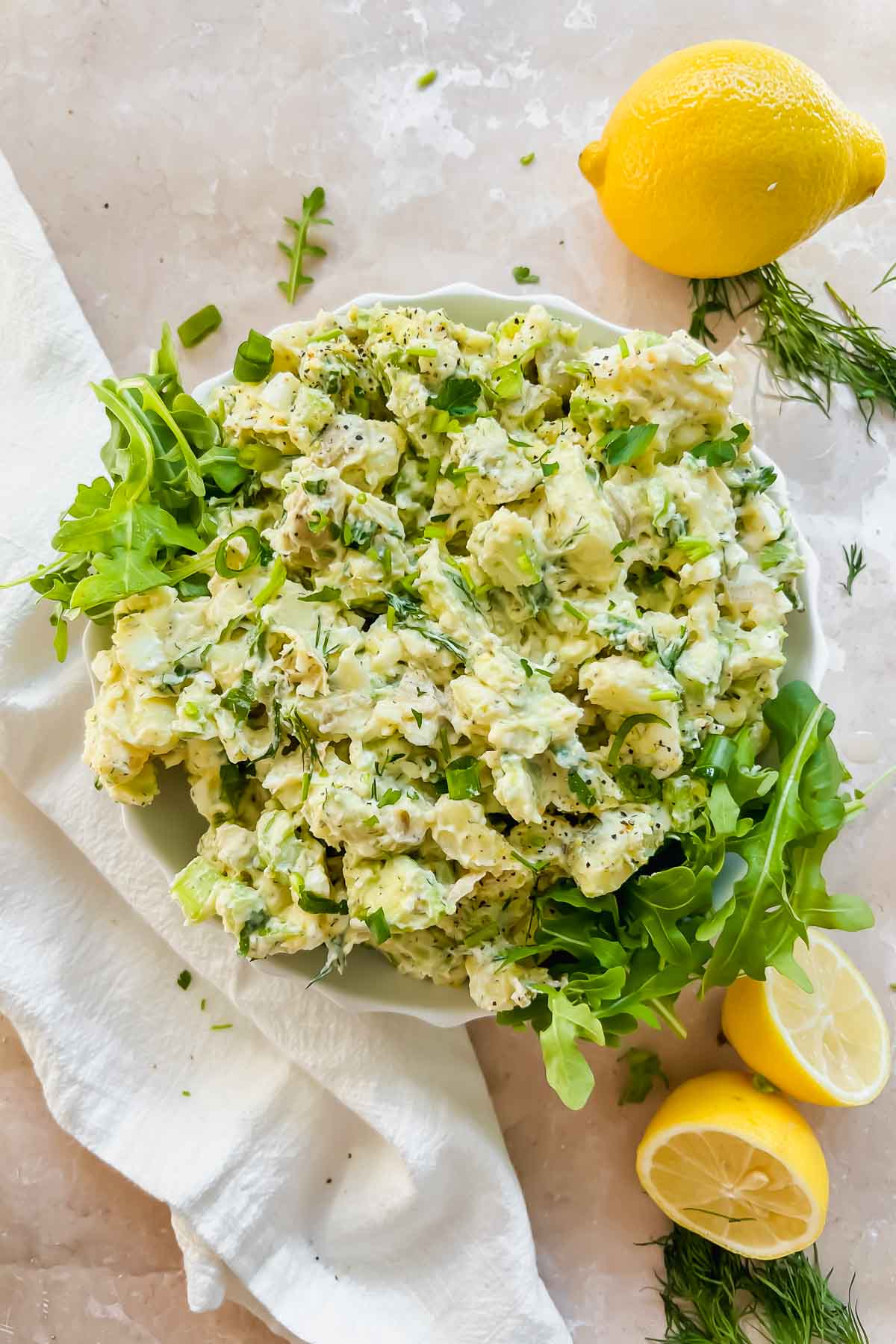 creamy healthy lemon dill potato salad mixed together over arugula in white bowl.