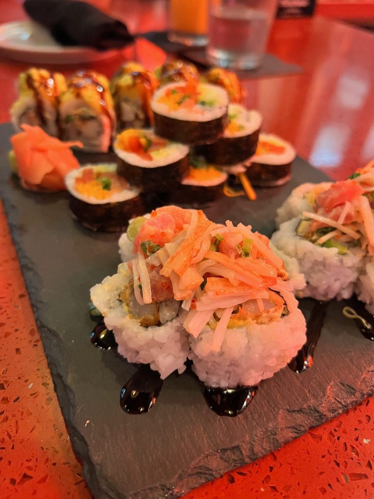 slate board filled with three rolls of sushi and topped with eel sauce. 