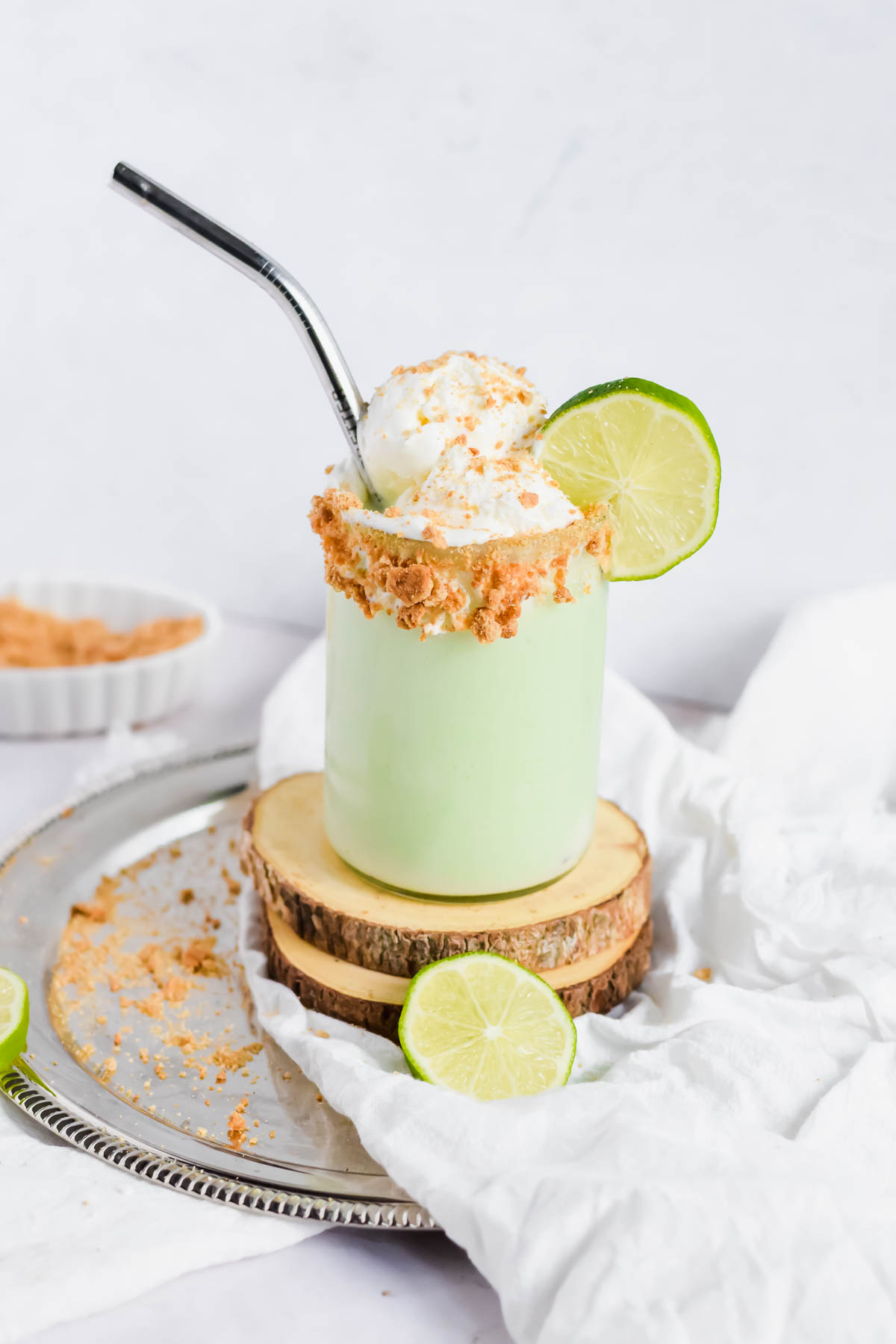 Key Lime Pie Milkshake topped with Cool Whip, crumbled graham cracker and a slice of lime with a metal straw.
