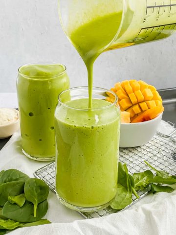mango spinach smoothie being poured into glass cup.