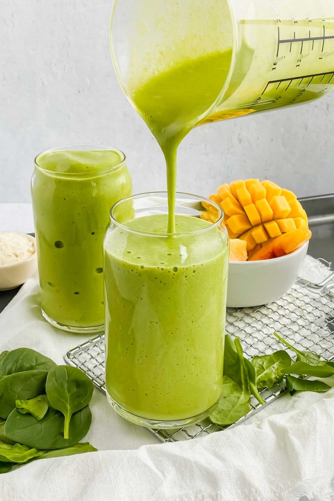 mango spinach smoothie being poured into glass cup.
