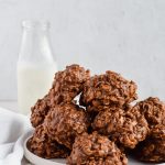 Pile of No Bake Oatmeal Cookies without Peanut Butter on a plate with a jug of milk in background.