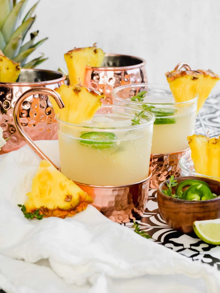 Two Pineapple Moscow Mules garnished with fresh pineapple and jalapeno slices.