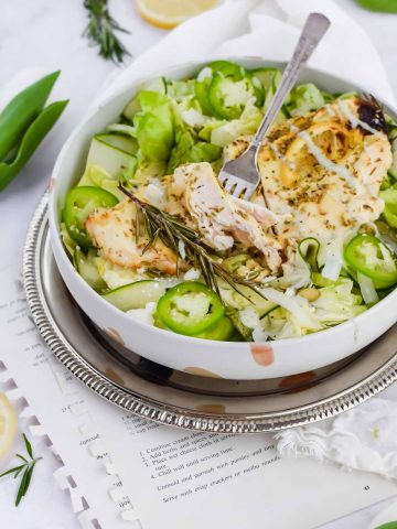 vibrant green goddess salad in white bowl on silver framed plate, white tulip surround and lemon slices.