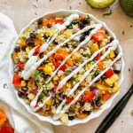 black bean couscous salad topped with fresh mexican crema in a white ceramic bowl.