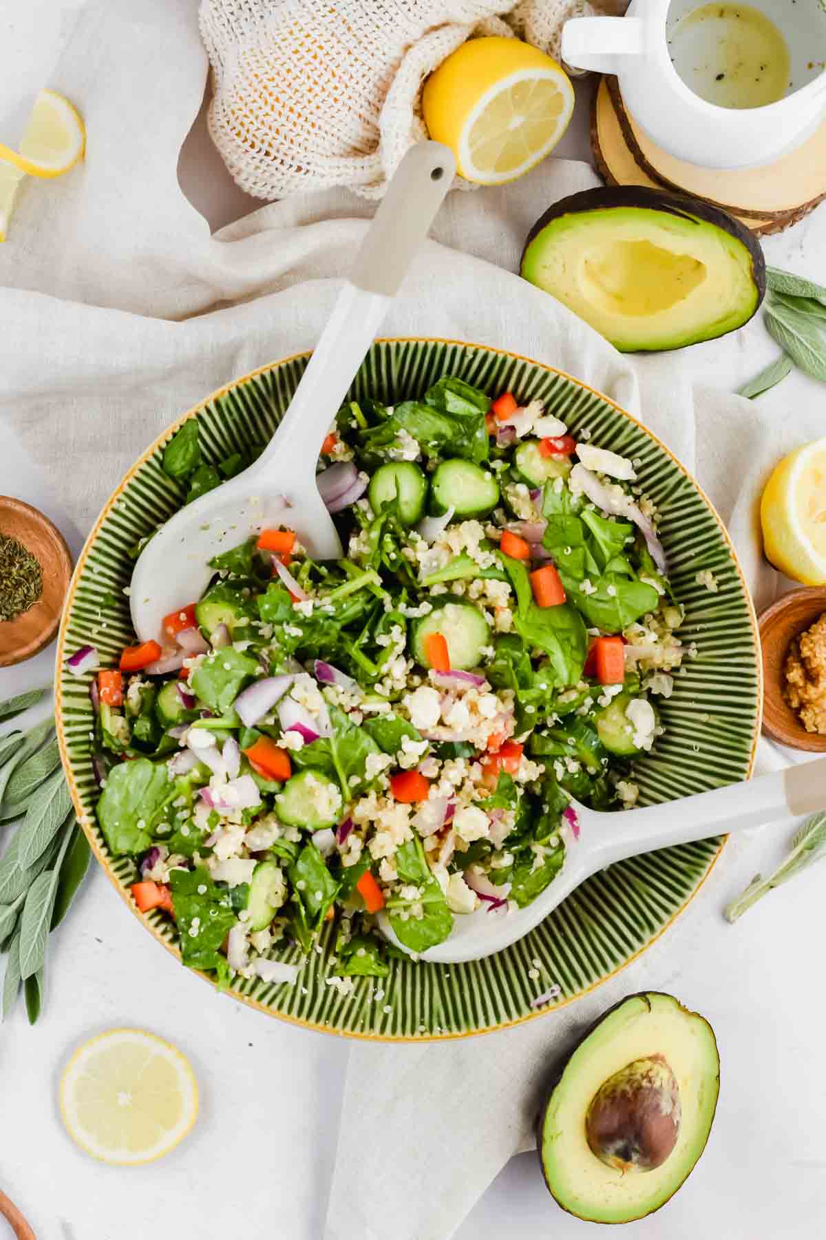 tossed salad in green salad bowl garnished with lemon slices, avocado, and olive oil.
