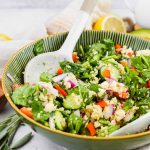 tossed spinach quinoa salad loaded with veggies in green salad bowl and white ceramic tongs.
