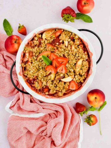 baked strawberry apple crisp in white pie dish toped with fresh strawberry slices.