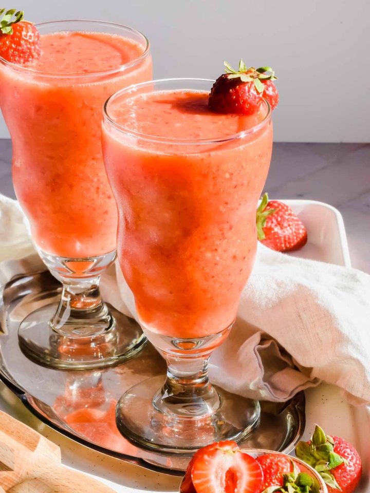 two frozen strawberry mango daiquiri cocktails in glasses garnished with a fresh strawberry.
