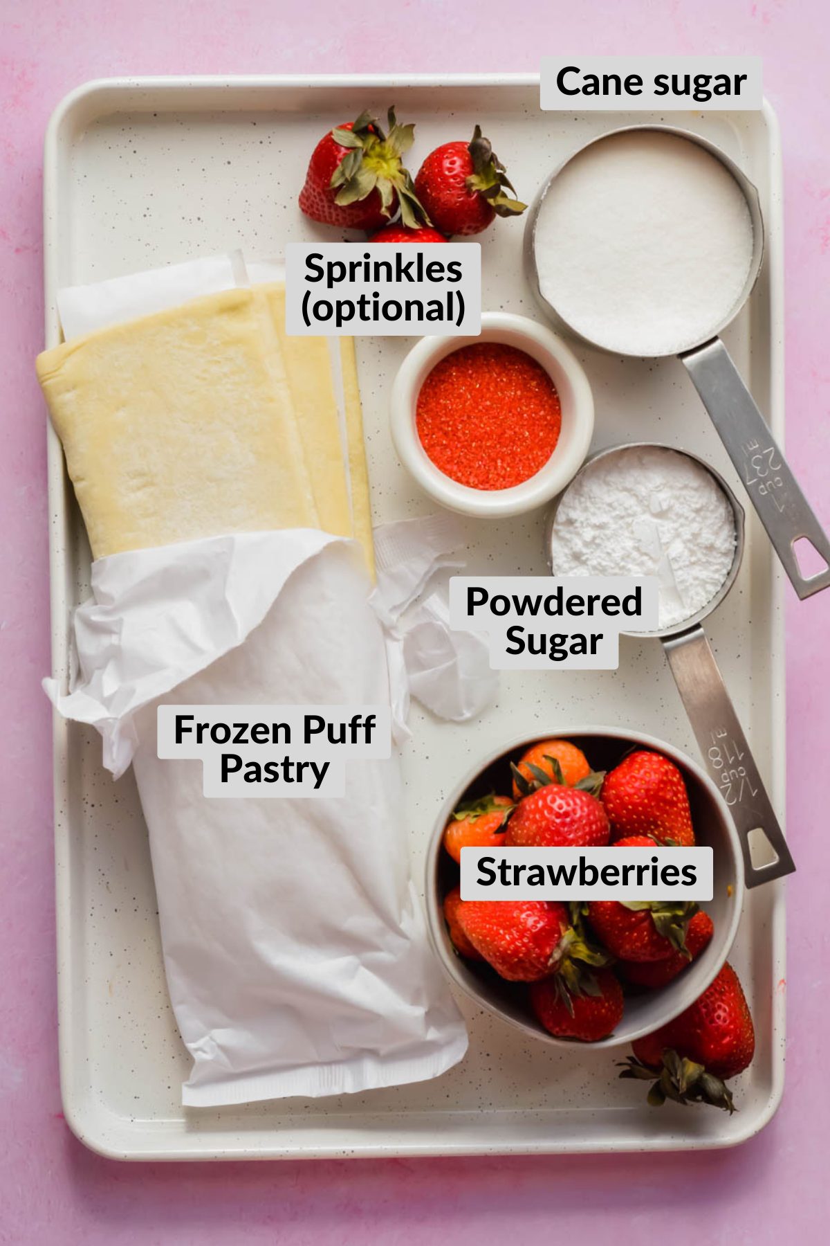 Ingredients for frosted strawberry pop tarts on white baking tray on pink background.
