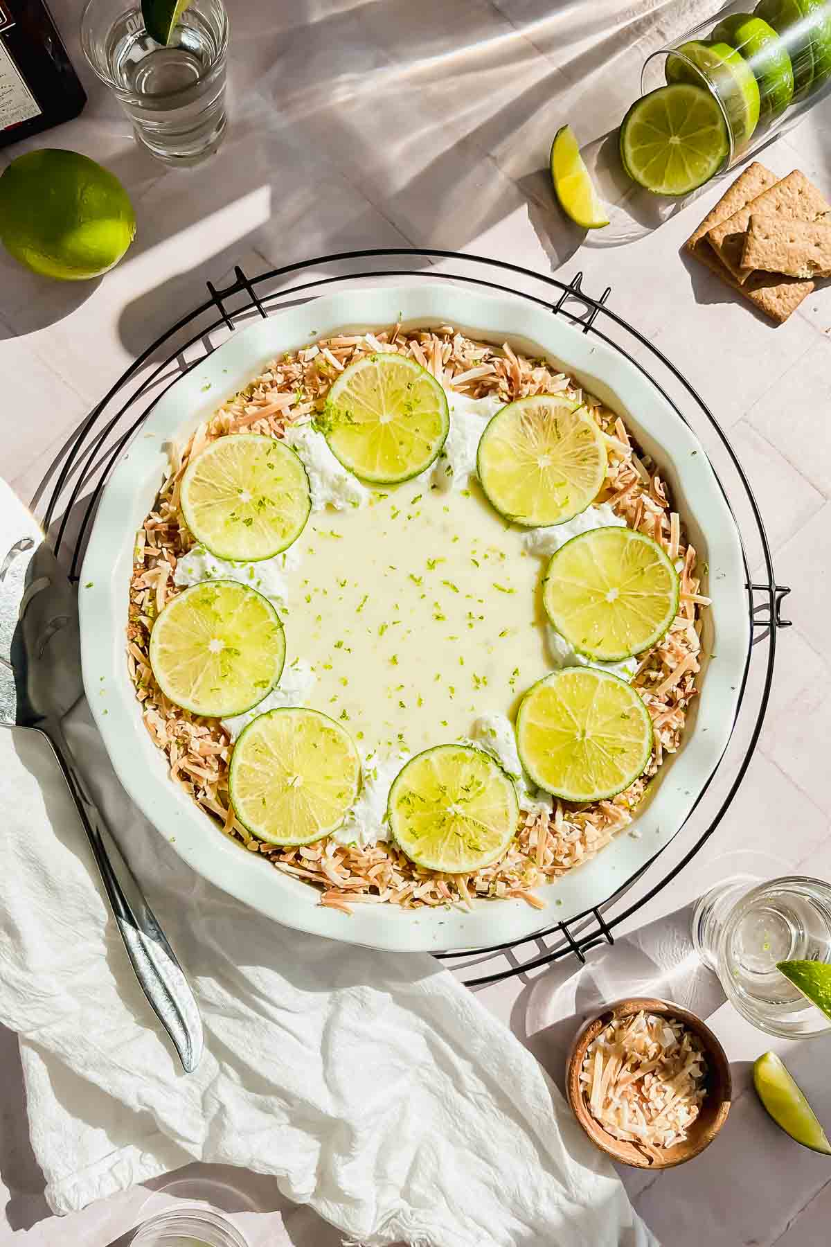 tequila key lime pie garnished with toasted coconut and lime slices in white baking dish.