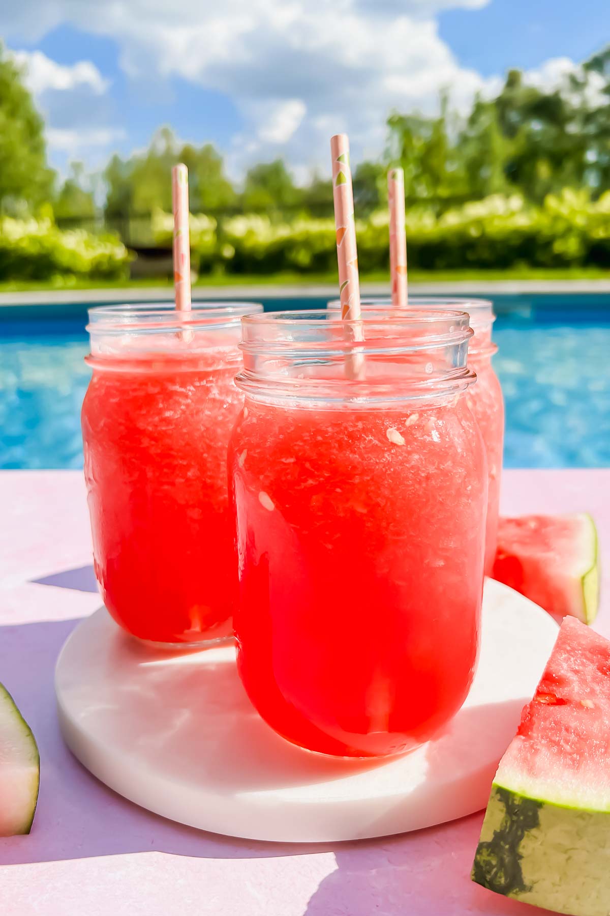 three watermelon vodka slushies in mason jars on white coaster.