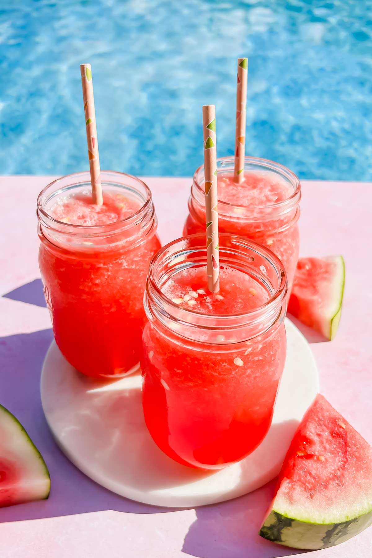 three watermelon vodka slushies in mason jars on white coaster.
