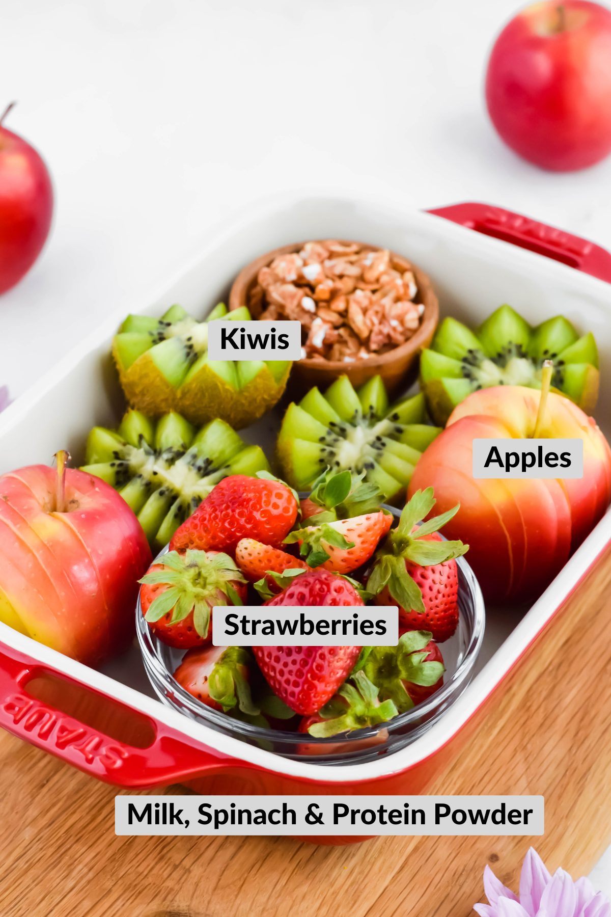 Freshly sliced apples and kiwi, fresh strawberries, and granola placed in a baking dish.
