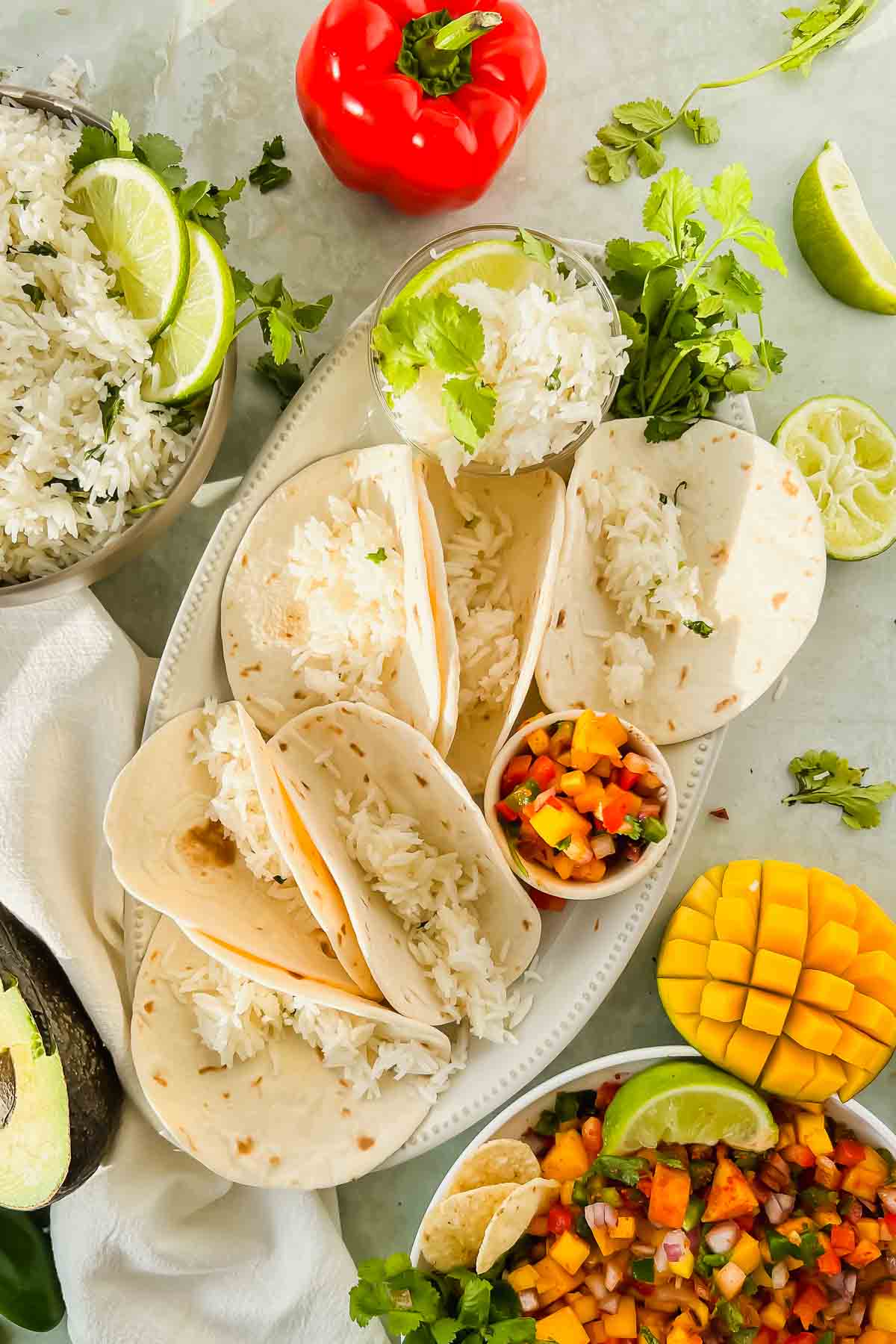 6 flour tortilla shells filled with rice on white serving plate surrounded by taco toppings.