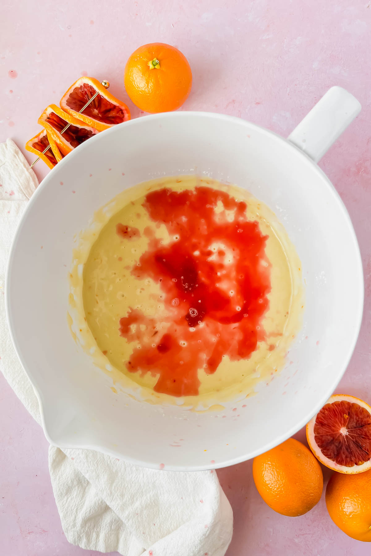 blood orange olive oil cake batter mixed in white mixing bowl with blood orange juice added on top.