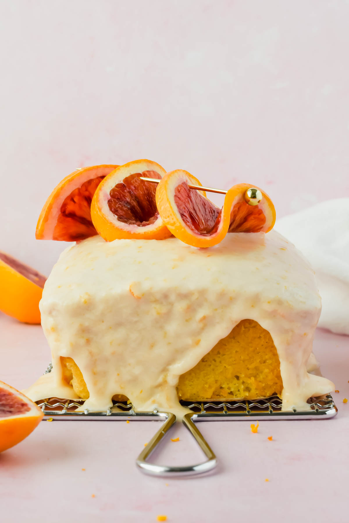 blood orange olive oil cake with white glaze topped with orange slices on wire rack.
