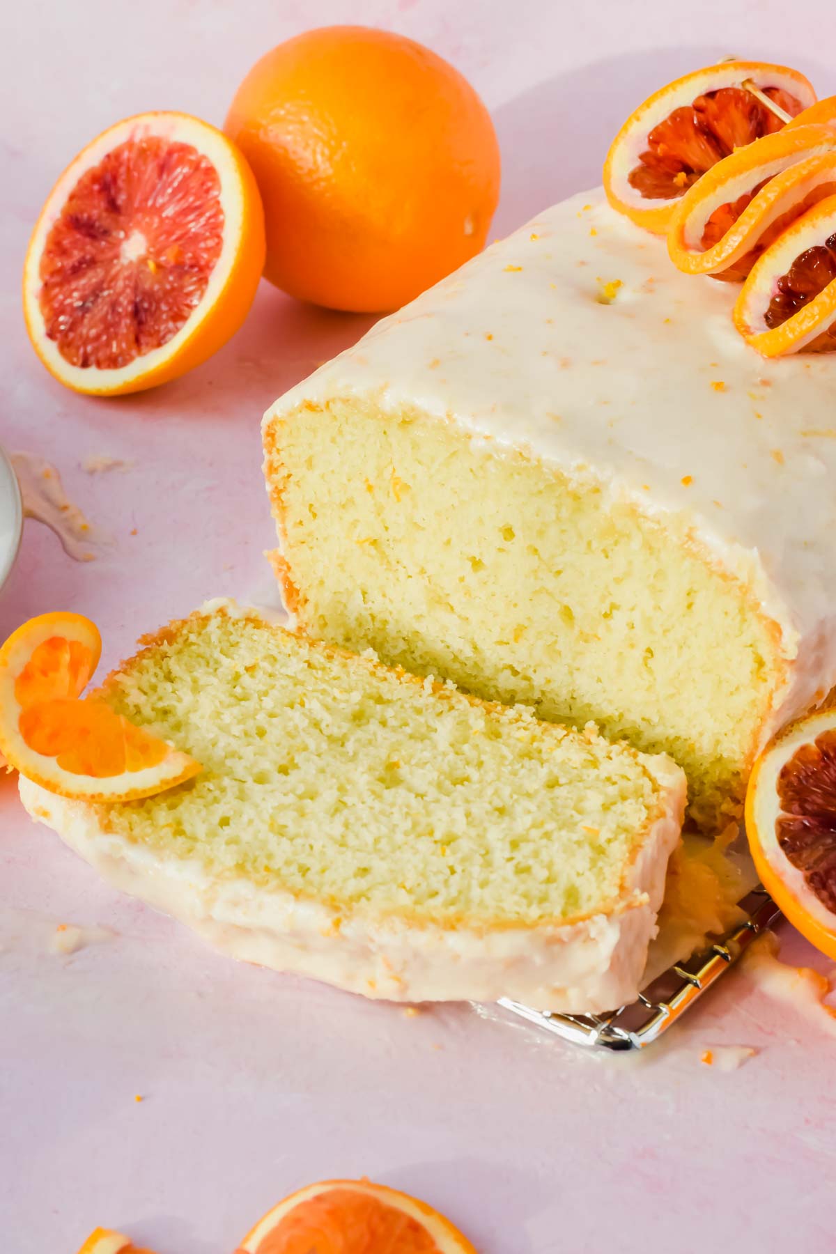 sliced blood orange olive oil cake with white glaze surrounded by orange slices.