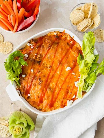 baked healthy buffalo chicken dip plated with colorful vegetables and crackers.