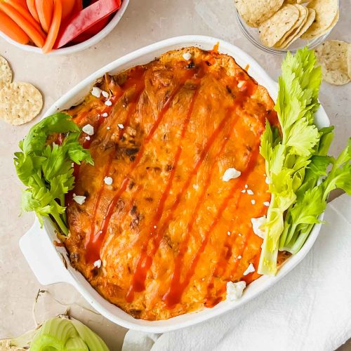 baked healthy buffalo chicken dip plated with colorful vegetables and crackers.
