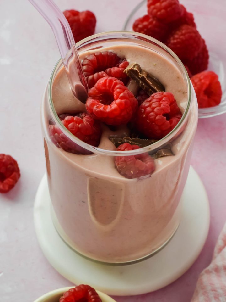 chocolate raspberry smoothie topped with fresh raspberries and chocolate chunks in glass with straw.