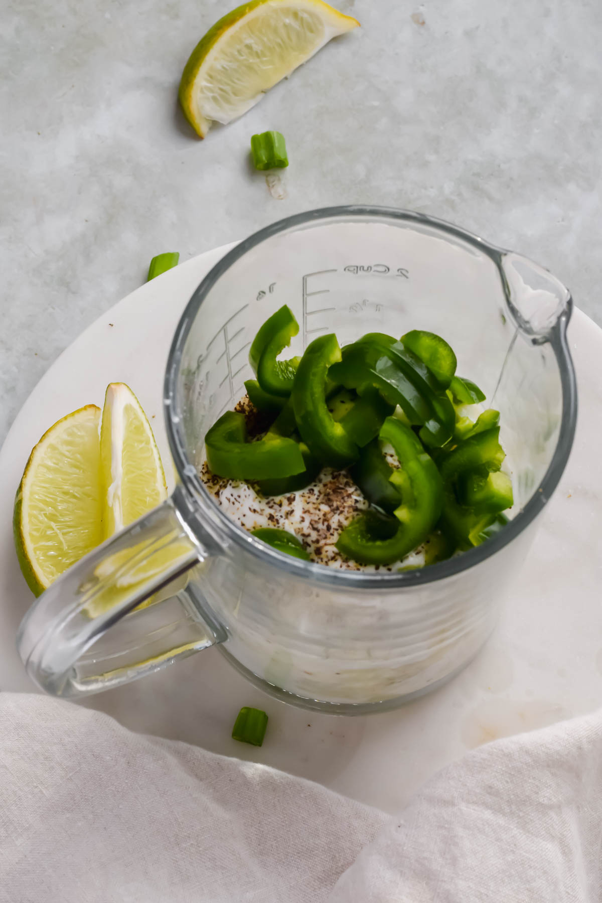 jalapenos and herbs added to yogurt dressing mixture in glass measuring cup. 