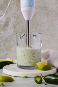 immersion blender in glass measuring cup blending creamy jalapeno sauce.