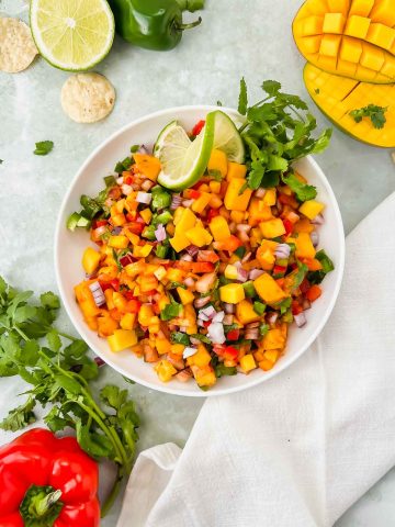 ceramic bowl filled with fresh mango salsa and chips with greenery around it.