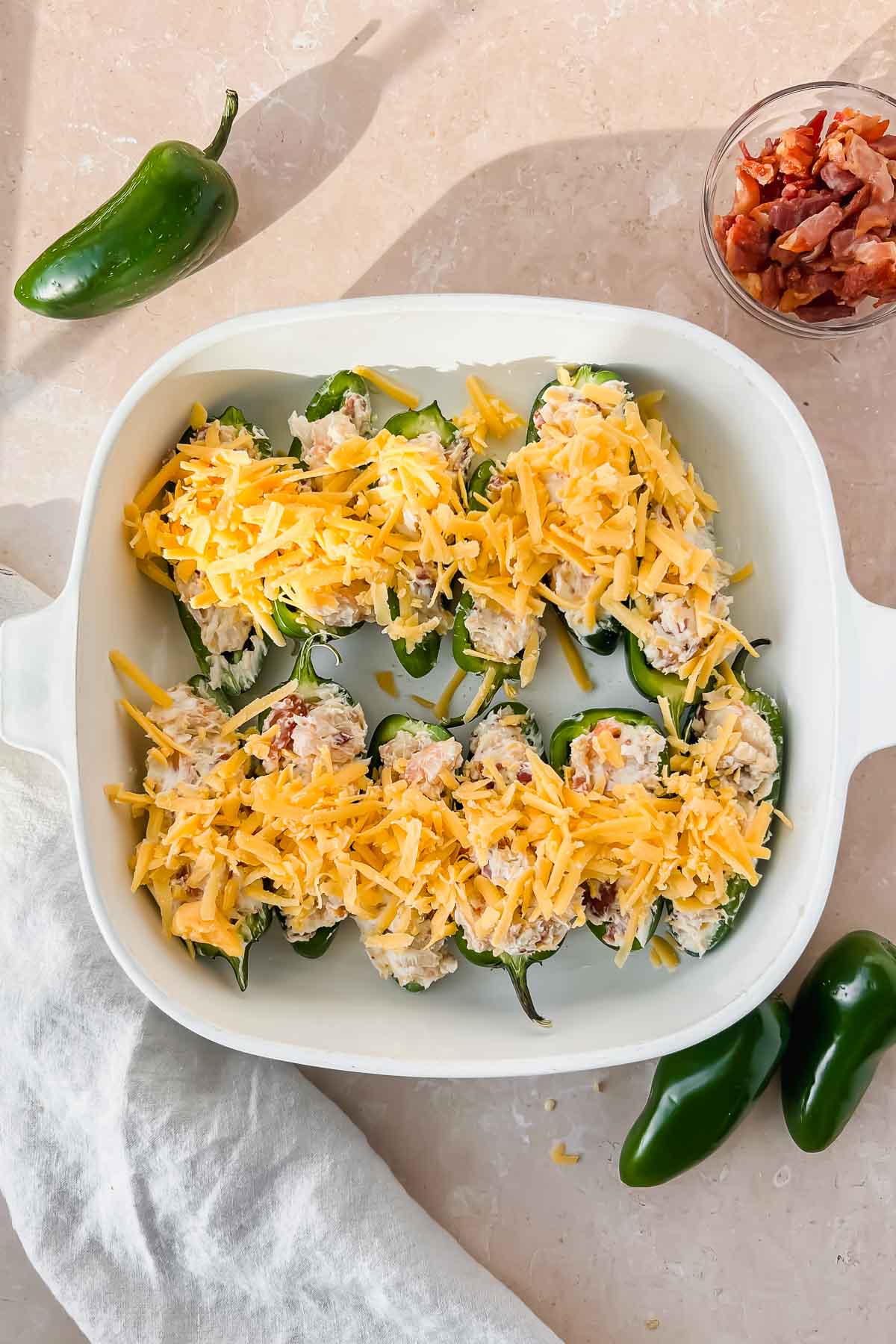 raw jalapeño shrimp poppers topped with shredded cheese arranged in white baking dish.