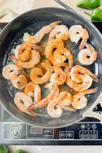 Shrimp with tails on cooking in skillet sprinkled with seasonings.