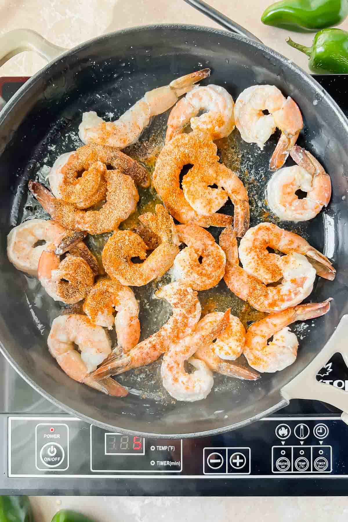 Shrimp with tails on cooking in skillet sprinkled with seasonings.