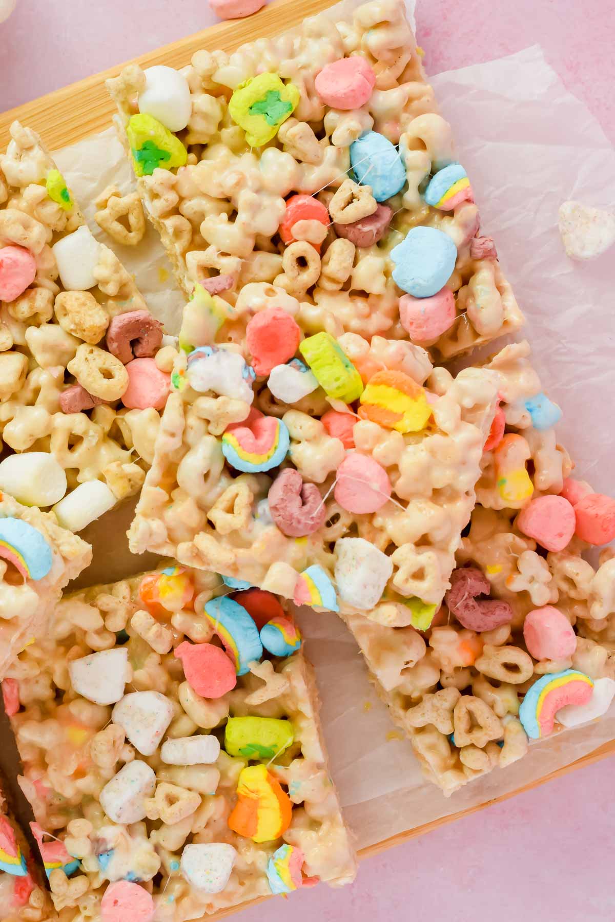 stacked lucky charm rice krispie treats cut into squares on white parchment.