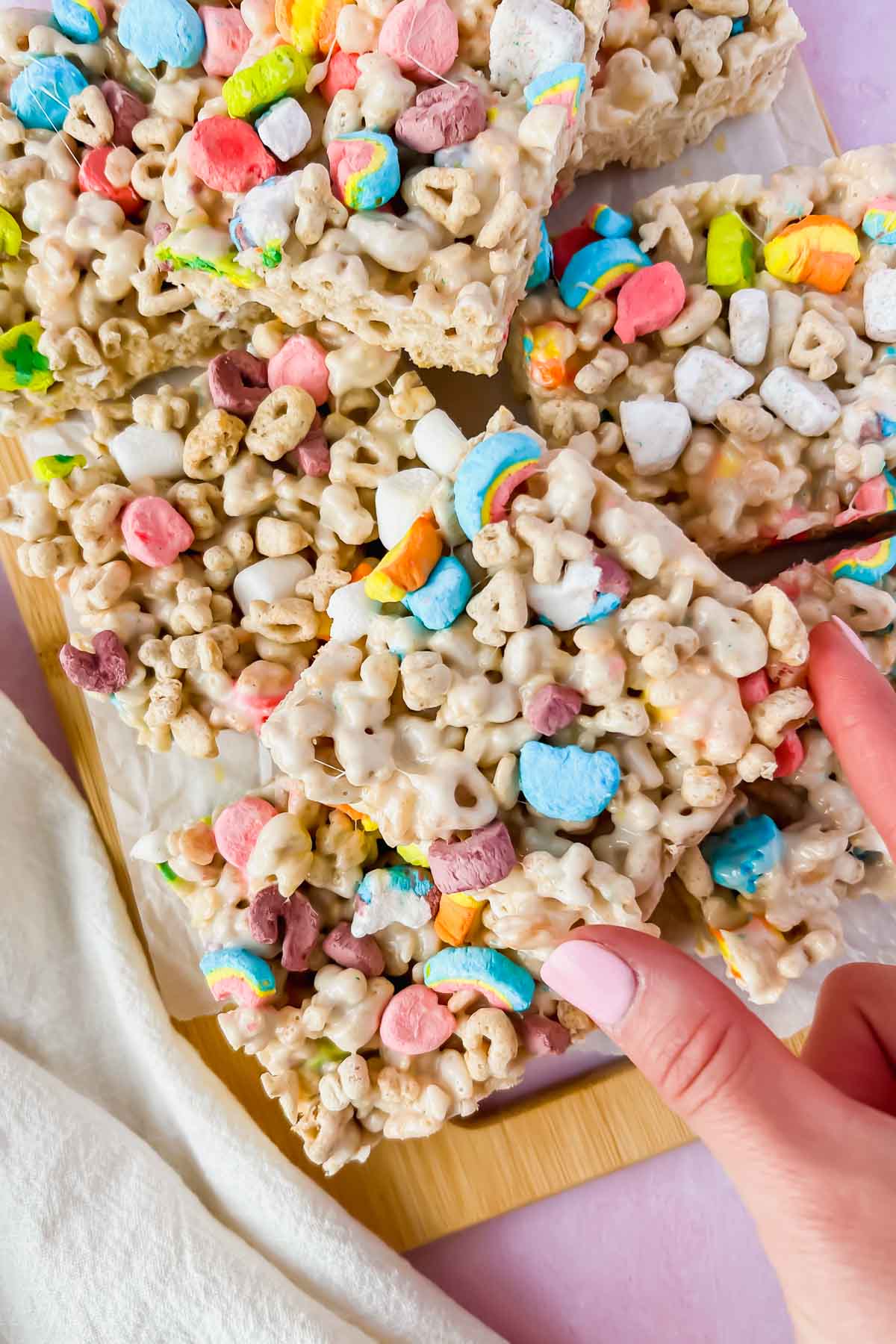 lucky charm rice krispie treats cut into squares with hand picking one up.
