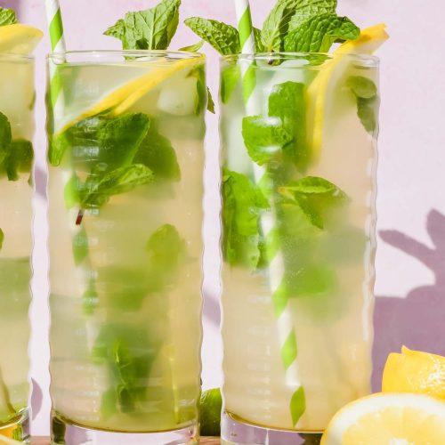skinny lemonade mojitos in tall ribbed glasses garnished with fresh lemons, mint, and a green and white striped straw.