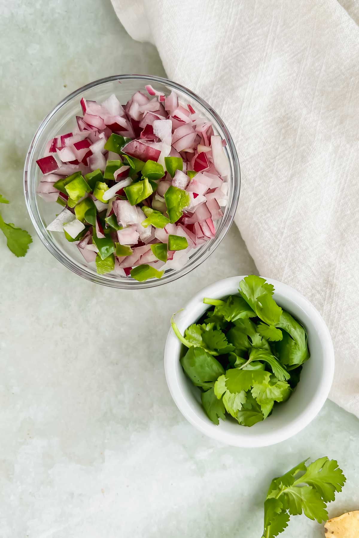 two bowls filled with diced red onions and cilantro on green background with white linen.