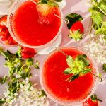 overhead shot of two strawberry martinis with sugared rim and garnished with fresh strawberry on gold skewer.