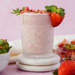 strawberry shortcake smoothie in vintage glass topped with fresh strawberries on pink background.