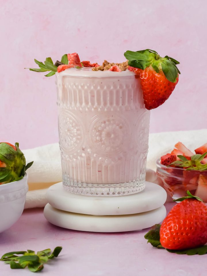 strawberry shortcake smoothie in vintage glass topped with fresh strawberries on pink background.