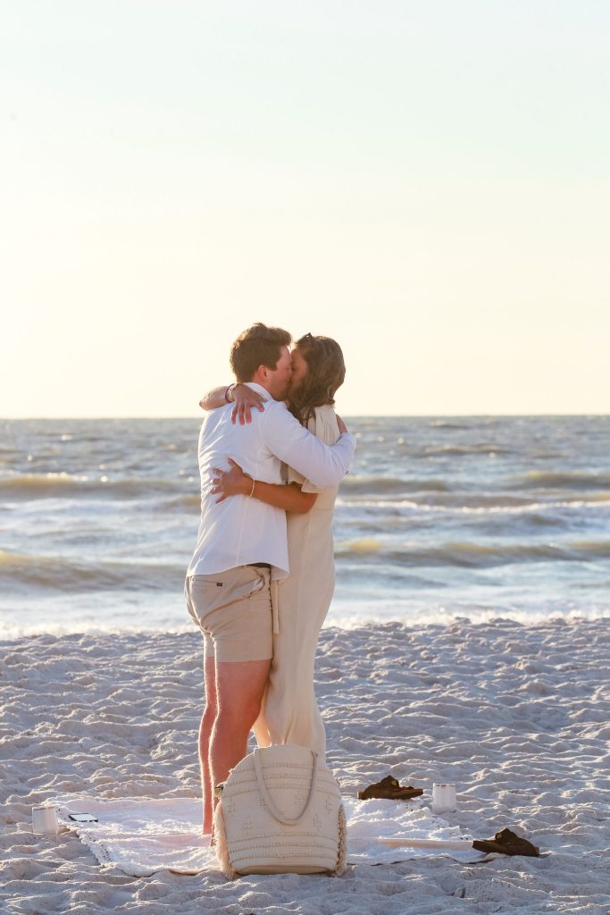 man and woman hugging on the beach at sunset after proposal.
