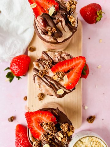 three glasses filled with brownie batter overnight oats and topped with fresh strawberries.