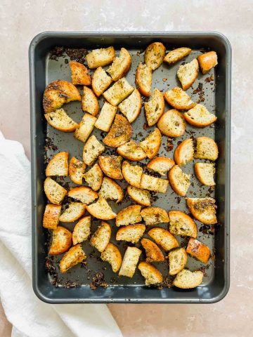 metal sheet pan with cooked french bread croutons on stone background.