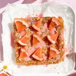 baked grapefruit bars on white parchment topped with grapefruit slices and pink glaze beside grapefruit slices on light pink background.