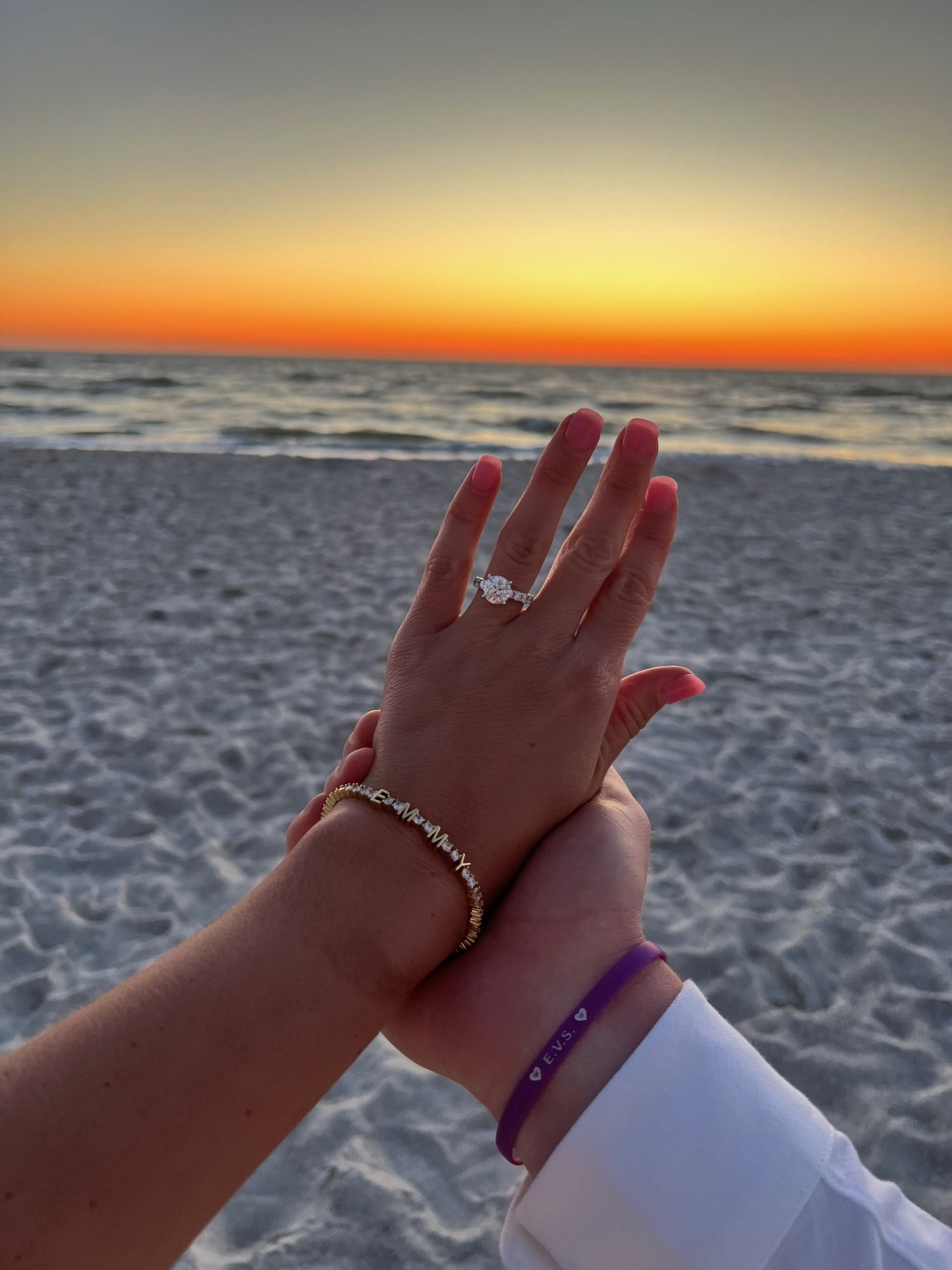 Hands holding together with engagement ring and sunset in background. 