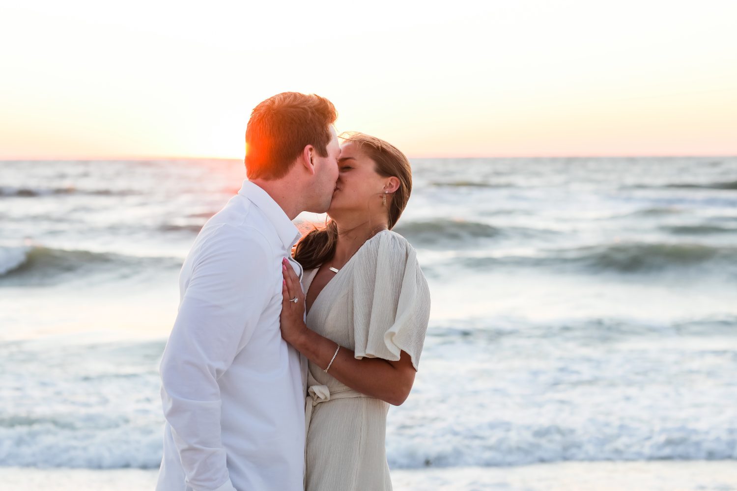 couple kissing in front of the ocean with a sunset in the background. 