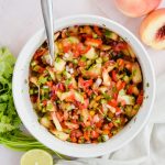 jalapeno peach salsa tossed in large white mixing bowl with silver spoon in bowl.
